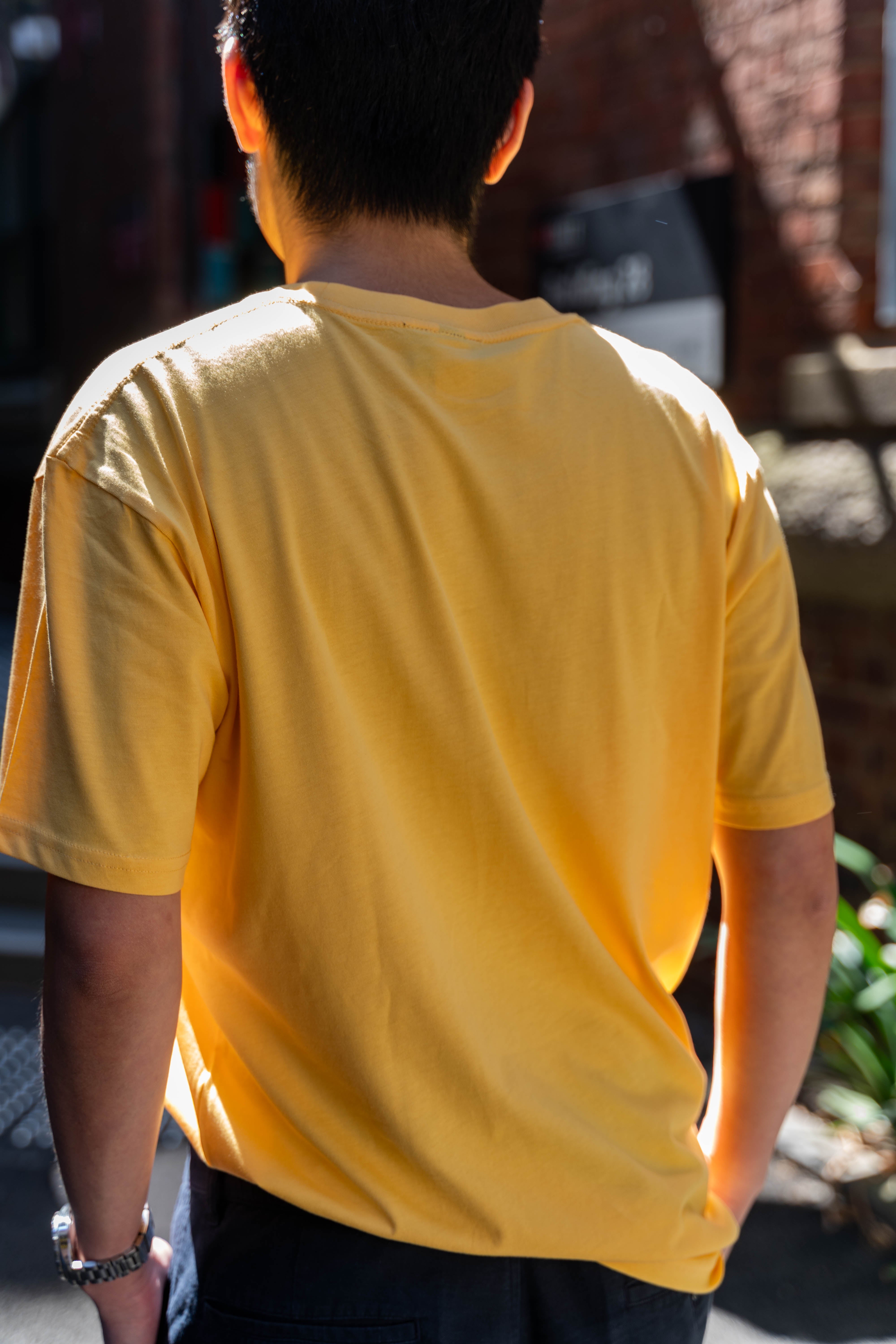 Model viewed from the back in the limited edition yellow Pride Unity Tee from RMIT Store, highlighting the tee's solid colour and relaxed fit.